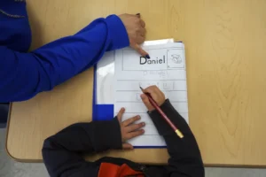 (Easterseals Head Start program teaching assistant Tania Ortiz helps a student practice writing his name, Jan. 29, 2025, in Miami. (AP Photo: Rebecca Blackwell, File)