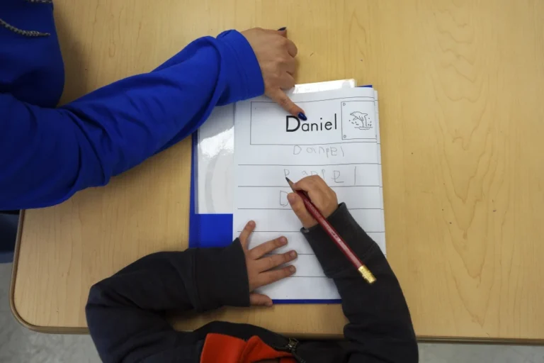 (Easterseals Head Start program teaching assistant Tania Ortiz helps a student practice writing his name, Jan. 29, 2025, in Miami. (AP Photo: Rebecca Blackwell, File)