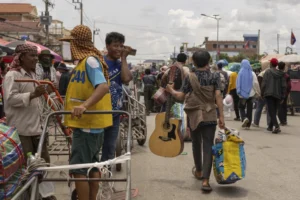 With a guitar in hand, a Cambodian migrant worker carries his belongings in Kamrieng, after crossing the Daung International Border Check Point between Cambodia and Thailand on Wednesday, Aug. 6, 2025. (AP Photo/Anton L. Delgado)