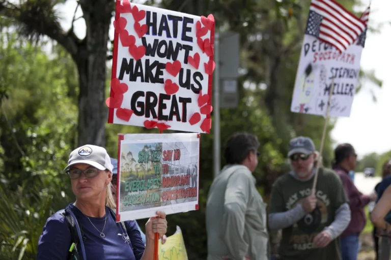 (A protester stands outside the migrant detention facility dubbed “Alligator Alcatraz” at the Dade-Collier Training and Transition Facility, Saturday, July 12, 2025, in Ochopee, Fla. AP Photo: Alexandra Rodriguez)