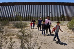(A family of five clamming to be from  Guatemala and a man stating  he was from Peru in pink shirt walk through the desert after crossing the border wall in the Tucson sector the US-Mexico border, Aug 29, 2023. AP Photo: Matt York)