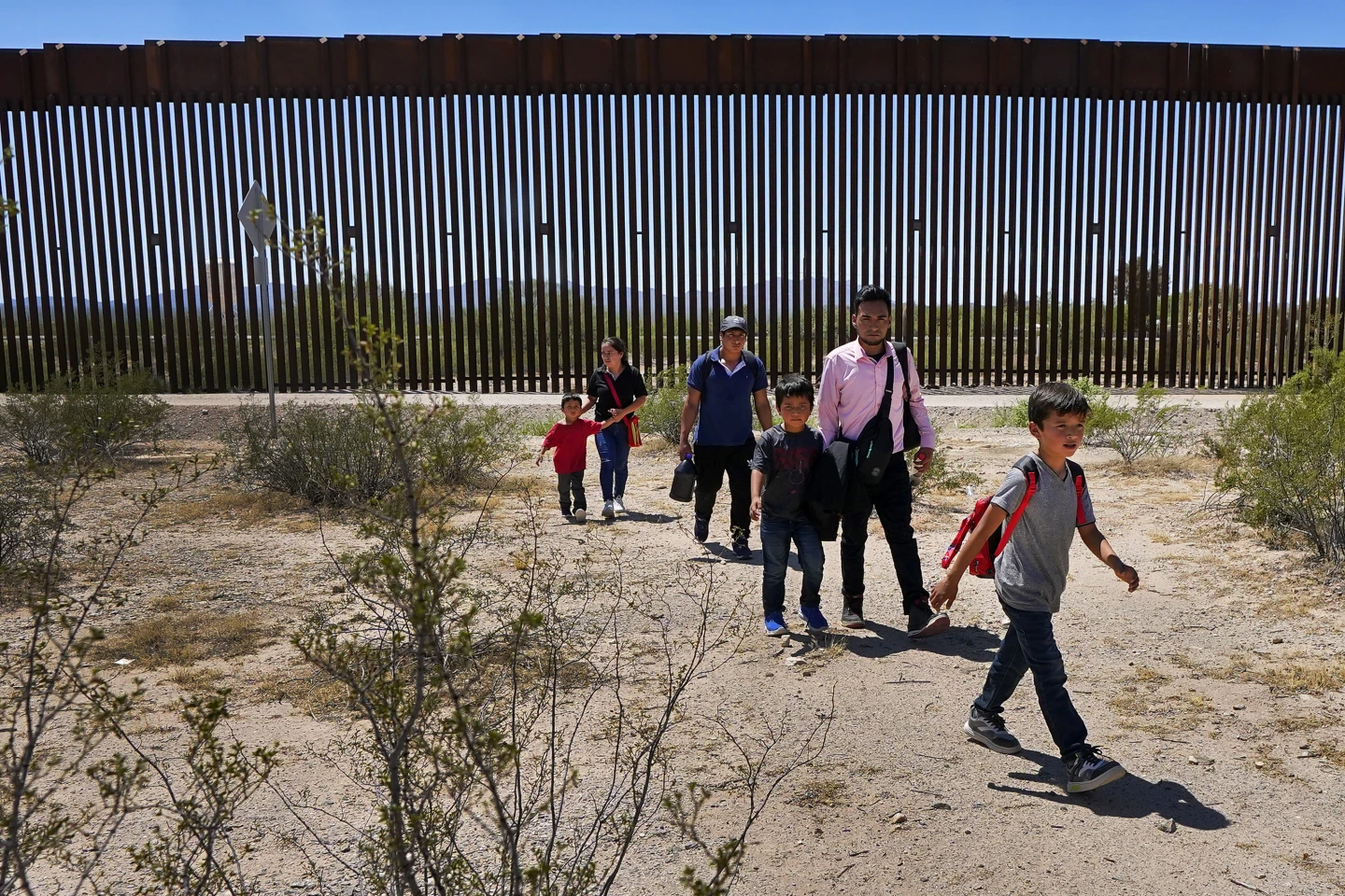 (A family of five clamming to be from  Guatemala and a man stating  he was from Peru in pink shirt walk through the desert after crossing the border wall in the Tucson sector the US-Mexico border, Aug 29, 2023. AP Photo: Matt York)