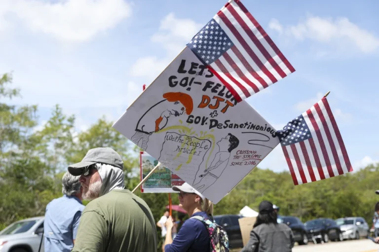 (A protester stands outside the migrant detention dubbed “Alligator Alcatraz” at the Dade-Collier Training and Transition Facility, Saturday, July 12, 2025, in Ochopee, Fla. AP Photo: Alexandra Rodriguez)