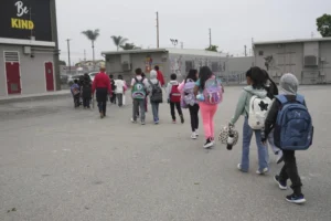 (Students and family members are escorted into school on the first day of school Thursday, Aug. 14, 2025, in Los Angeles. AP Photo: Marcio Jose Sanchez)