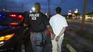(An Immigration and Customs Enforcement officer escorts a person in handcuffs.  File photo courtesy of Immigration and Customs Enforcement)