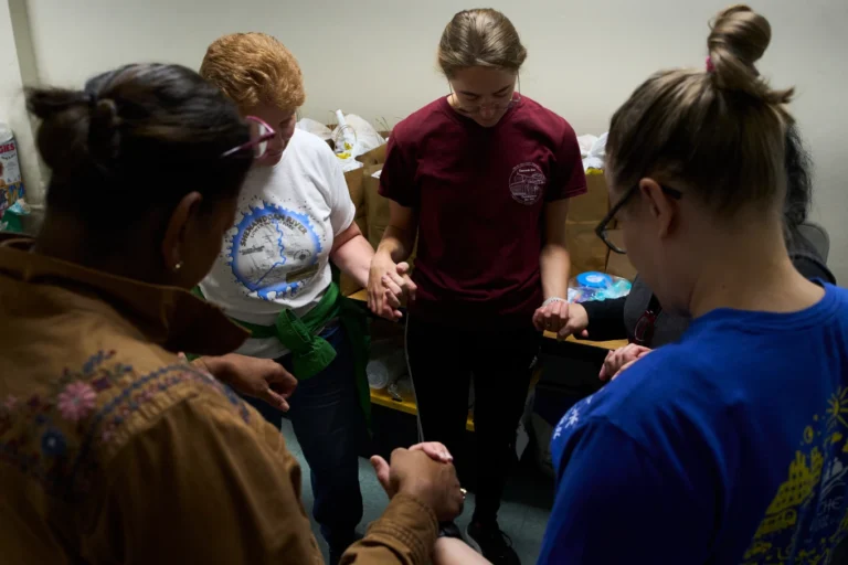 (Parishioners of the Shrine of the Sacred Heart and volunteers pray in the church’s basement before delivering donated food to families who are afraid to leave their homes. AP Photo: Luis Andres Henao)