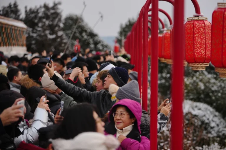 (People view the snow-covered Forbidden City from a pavilion with lantern decorations at Jingshan Park in Beijing on Sunday.  AP Photo: Andy Wong)