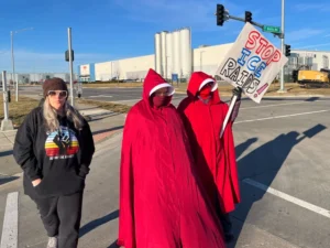 (Melissa Kane, a self-described worried mother, joins protestors clad in red cloaks inspired by the dystopian novel and TV series, “The Handmaid’s Tale,” as they protest outside a warehouse federal officials are touring to consider repurposing for an ICE detention facility, in Kansas City, Mo., Thursday, Jan. 15, 2026.  AP Photo: Heather Hollingsworth)