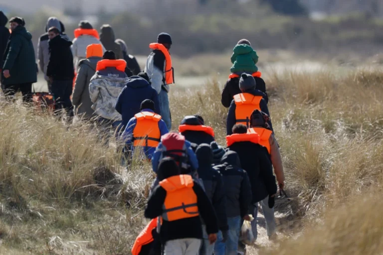 (Migrants trying to reach Britain, walk on a beach shore in Gravelines, northern France, Wednesday, March 18, 2026. AP Photo: Jean-Francois Badias)