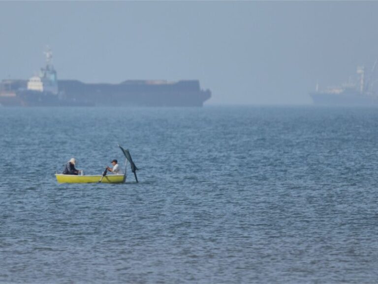 (Two men sit in a small boat on the water as cargo ships are anchored in the background in the Strait of Hormuz off Bandar Abbas, Iran, Monday, May 4, 2026. (Amirhosein Khorgooi/ISNA via AP)