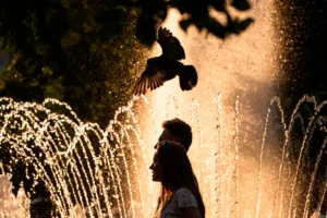 (A couple walks by a public fountain on a torrid day, as the National Weather forecaster issued an extreme heat code red warning for parts of the country, in the coming days in Bucharest, Romania, Saturday, June 27, 2026.  AP Photo: Andreea Alexandru)