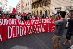 (People hold a banner in Italian reading "Skin and sweat have the same color, no deportation' during a march in Rome, June 13, 2026, to protest Italy's security and migration package, including a migrant "repatriation bonus" scheme criticized by opposition parties and legal groups as unconstitutional and ethically problematic.  AP Photo: Gregorio Borgia)