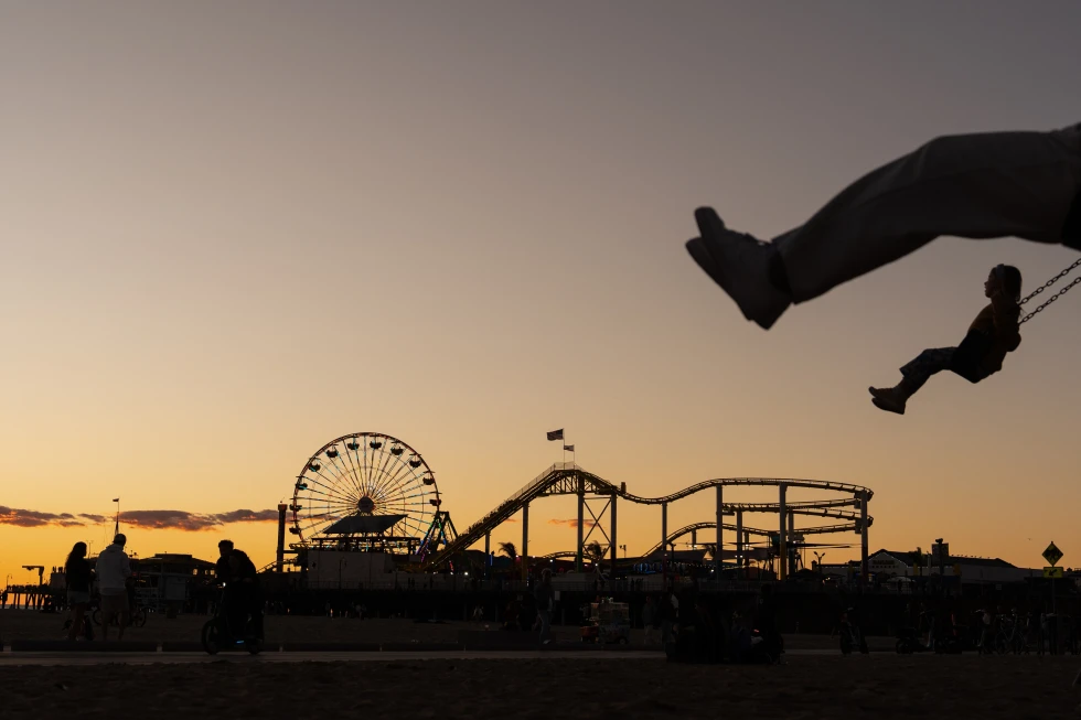 (Children swing in silhouette near the Santa Monica Pier, which displays the “End of the Trail” Route 66 sign in Santa Monica, Calif., Nov. 22, 2025.  AP Photo: Jae C. Hong)