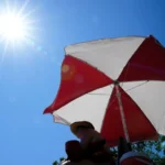 (The sun beams down on a lifeguard while she watches over a beach at Lake Harriet during an extreme heat warning, Monday, July 13, 2026, in Minneapolis.  AP Photo: Ellen Schmidt)