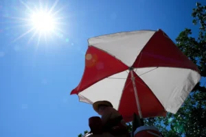 (The sun beams down on a lifeguard while she watches over a beach at Lake Harriet during an extreme heat warning, Monday, July 13, 2026, in Minneapolis.  AP Photo: Ellen Schmidt)