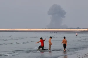 (Three boys play in the shallow waters of the Strait of Hormuz, as a plume of smoke rises from an explosion in the background, off Bandar Abbas, Iran, Monday, July 13, 2026. Photo: Razieh Poudat-ISNA via AP)