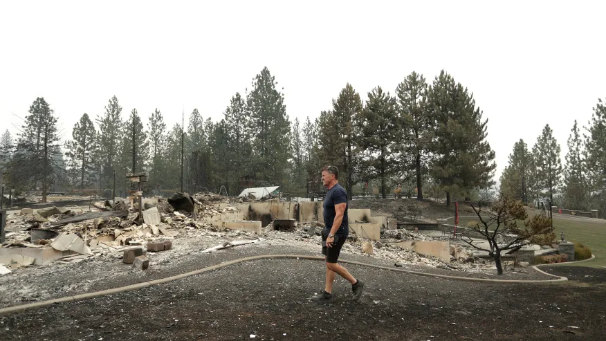 (Dan Munson walks in the backyard of his home on W. TIffany Ave. after it burned in a wildfire, Sunday, Aug. 2, 2026, in Spokane, Wash.  AP Photo: Young Kwak)