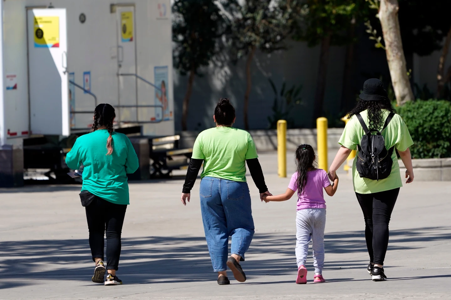 A child holds hands with workers at an emergency shelter for migrant children, July 2, 2021, in Pomona, Calif.  AP File Photo: Marcio Jose Sanchez, Pool)