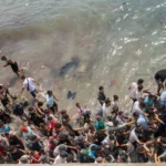 (People walk on a beach as they attempt to cross from the Moroccan northern town of Fnideq to the Spanish enclave of Ceuta, July 31, 2026. AP File Photo)