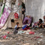 (A displaced Yemeni family sits beside a makeshift shelter along a roadside in Aden, Yemen, Sunday, Oct. 11, 2026.  AP Photo: Abdulnasser Alseddik)