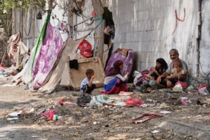 (A displaced Yemeni family sits beside a makeshift shelter along a roadside in Aden, Yemen, Sunday, Oct. 11, 2026.  AP Photo: Abdulnasser Alseddik)