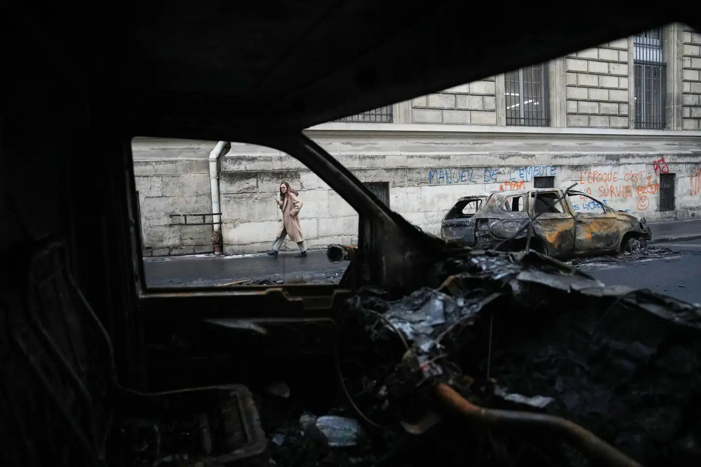 (A woman walks past burned-out cars after a quiet night Monday under curfew, the first since weekend protests over the cost of living turned into rioting and looting across France, in Paris, Tuesday, Oct. 20, 2026.  AP Photo: Christophe Ena)