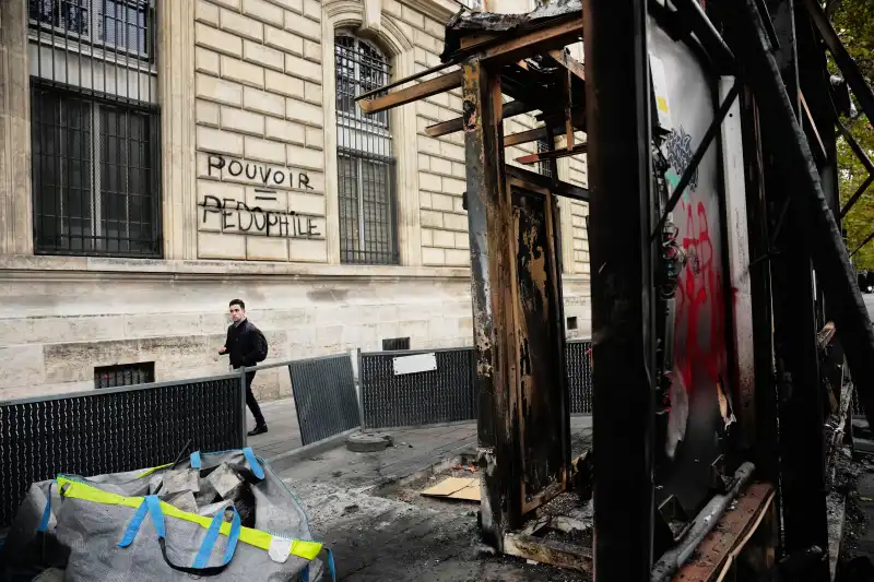 (A man walks past a burned-out structure next to the inscription in a wall ¨Power = Pedophilia¨ after the weekend protests over the cost of living turned into rioting and looting across France, in Paris, Wednesday, Oct. 21, 2026.  AP Photo: Teresa Suarez)