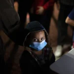 (An unaccompanied minor looks up as he waits to answer questions from a U.S. Border Patrol agent at an intake site after he was smuggled on an inflatable raft across the Rio Grande River, March 24, 2021, in Roma, Texas. (AP File Photo: Dario Lopez-Mills)