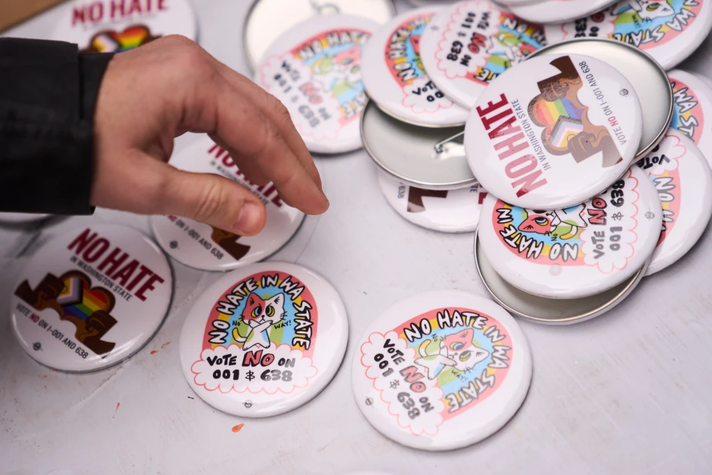 (A person picks up a button during a "No Hate in WA State" rally against multiple initiatives on the November ballot, including Washington State Initiative 638, which would prohibit transgender girls from competing in girls' sports, Saturday, Oct. 17, 2026, in Seattle. AP Photo: Lindsey Wasson)